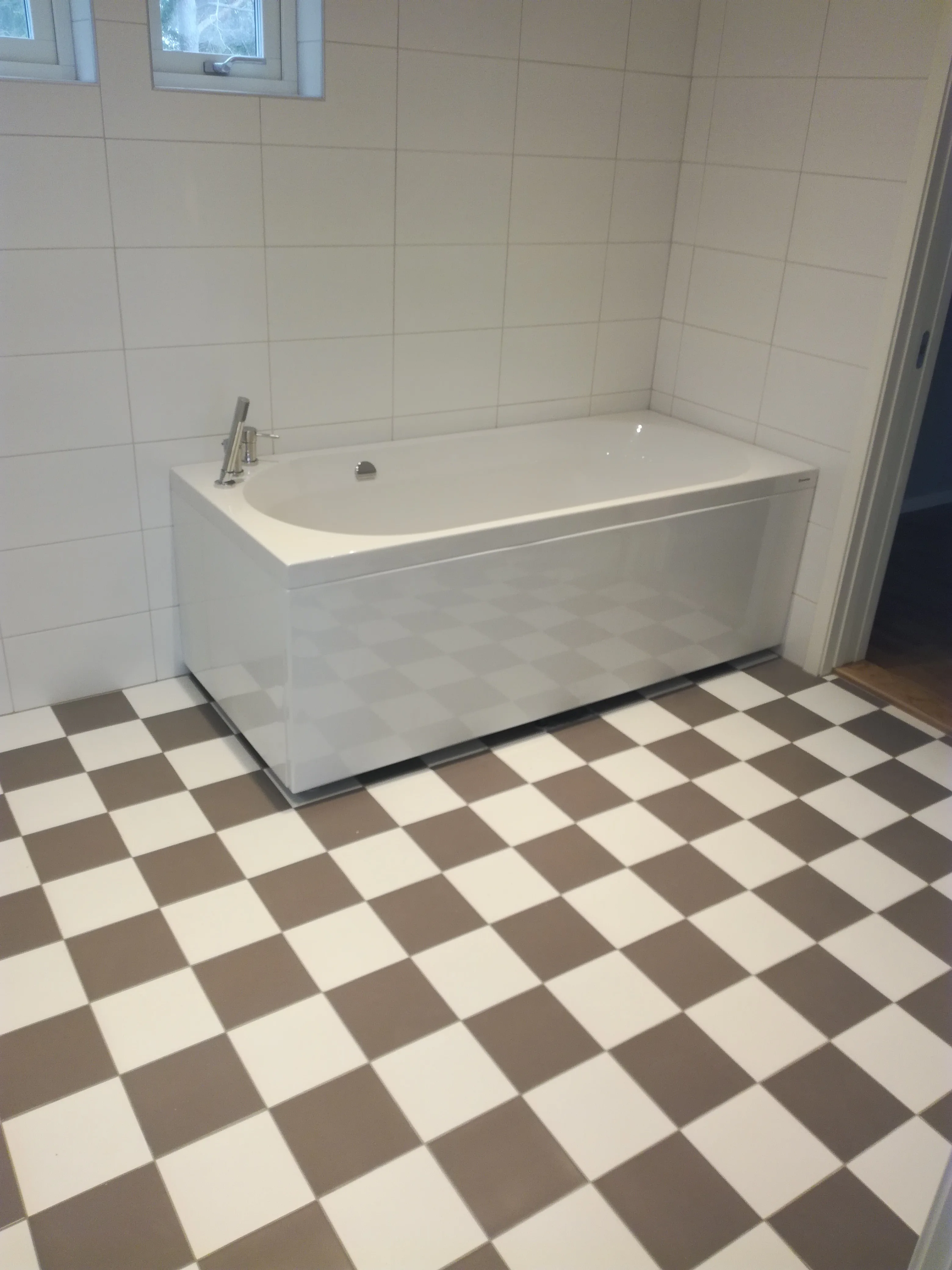 Renoverat badrum med vitt badkar och rutmönstrat golv