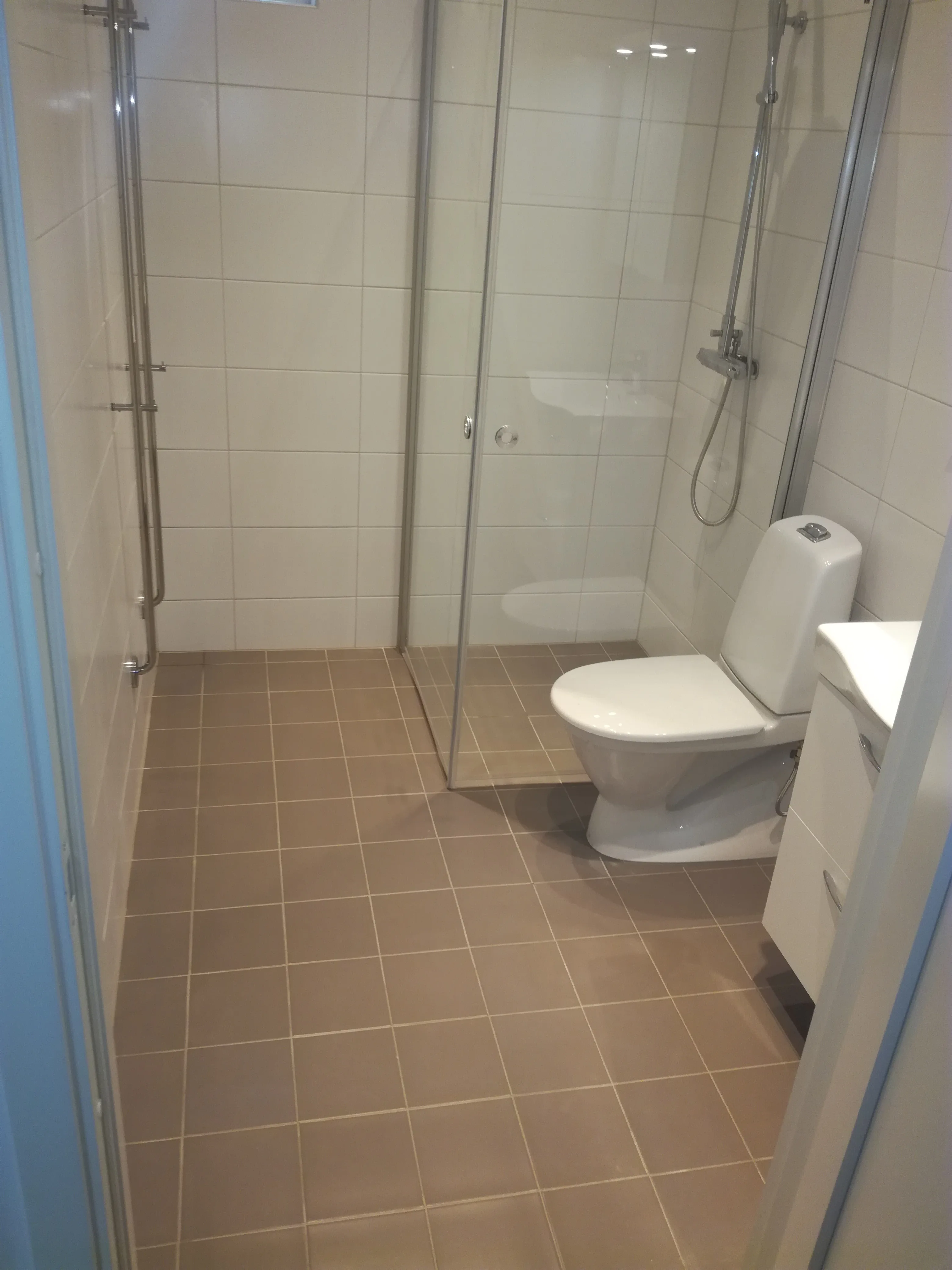 Renoverat badrum med glasdusch och bruna plattor