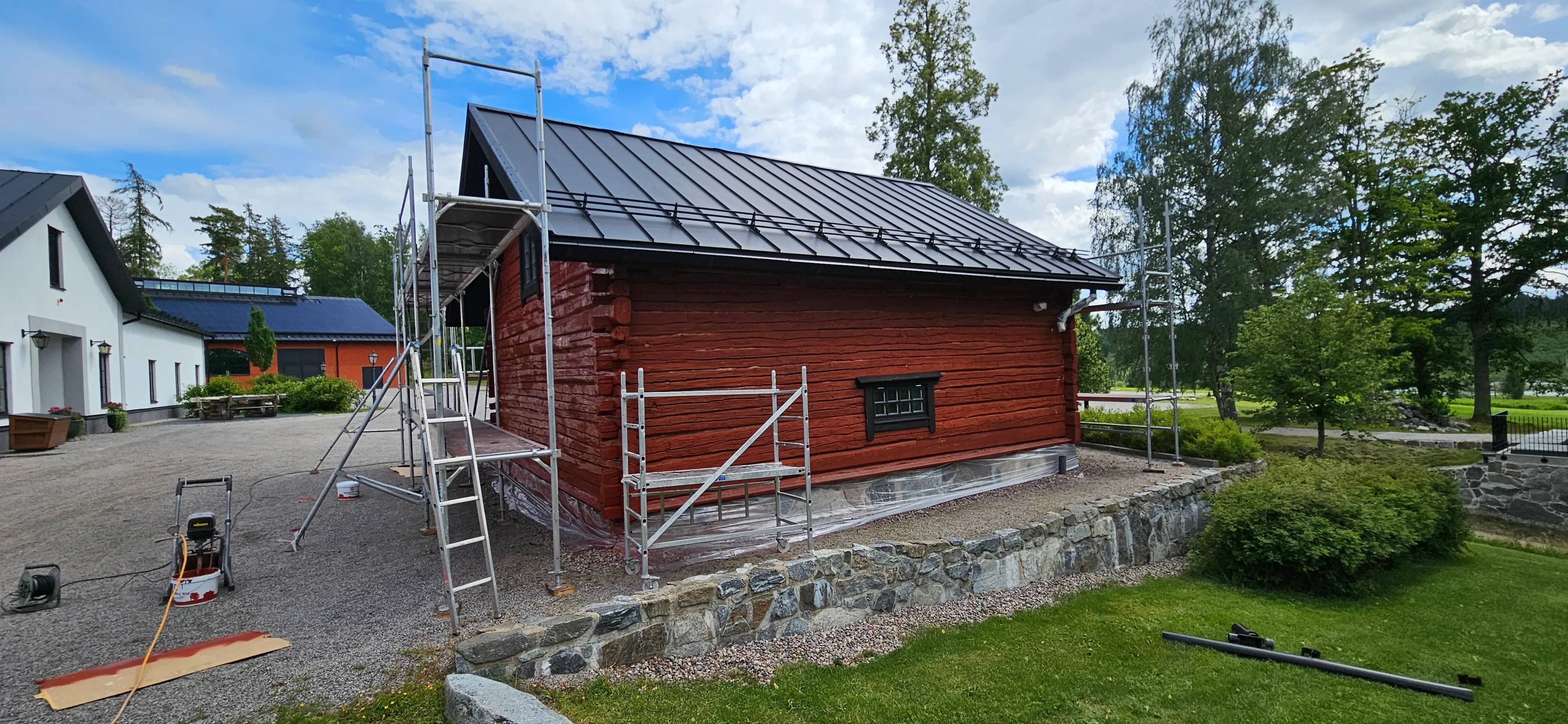 Fasadrénovering av ett rött hus med byggställningar och grönskande omgivning