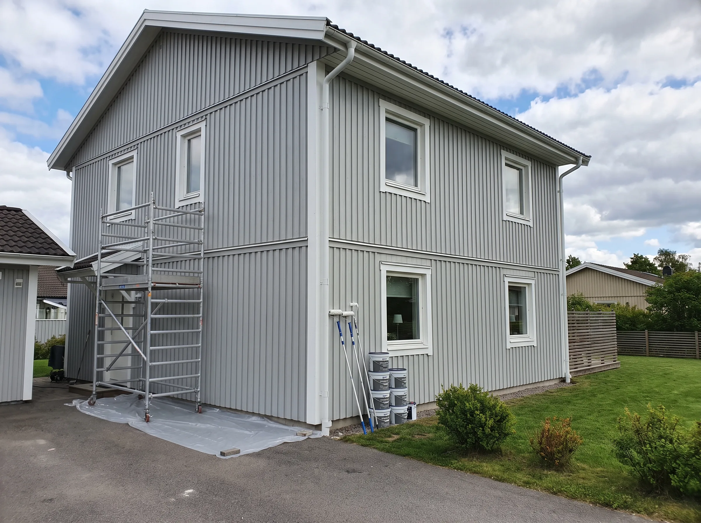 Fasadrenovering av ett hus med byggställning och färgburkar i förgrunden