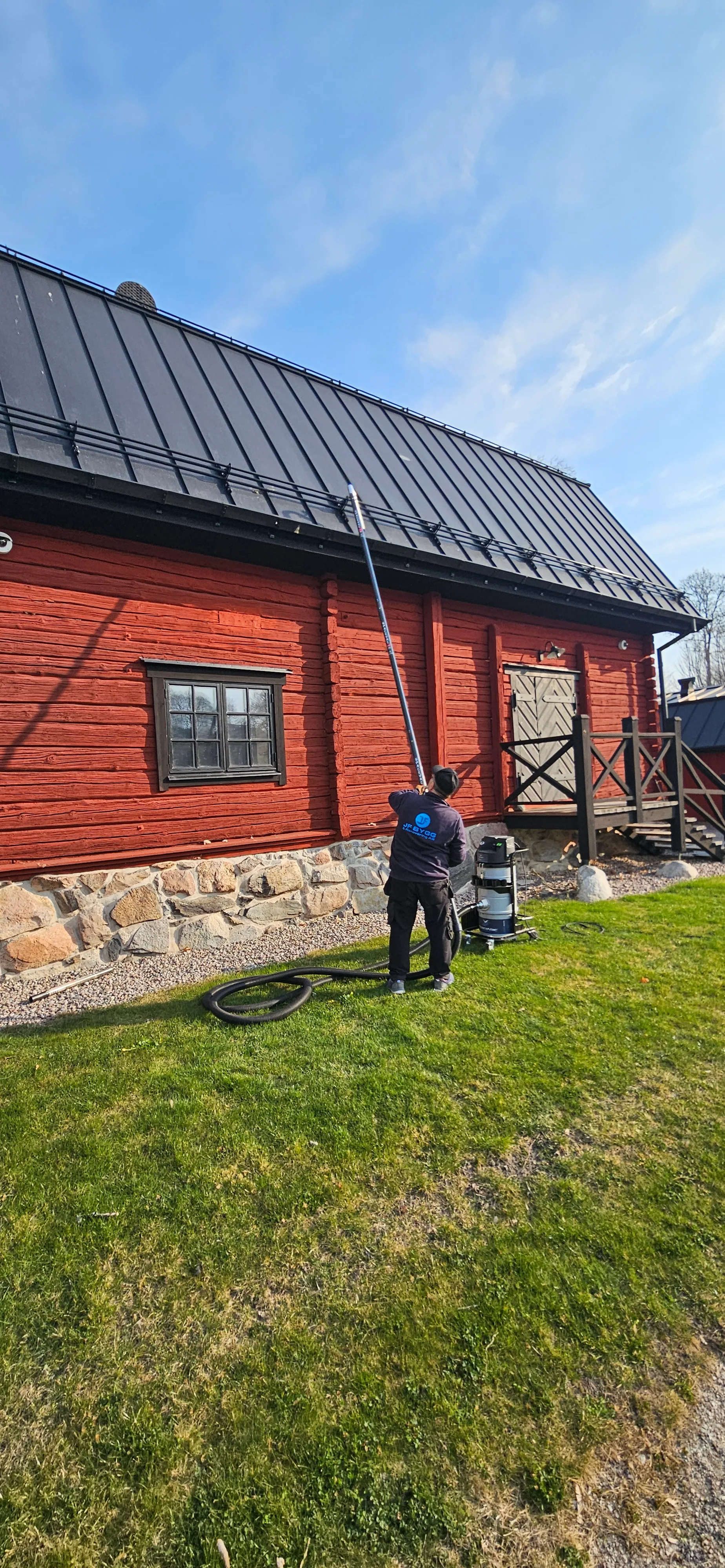 En person som utför fasadmålning på en röd byggnad med tak av plåt