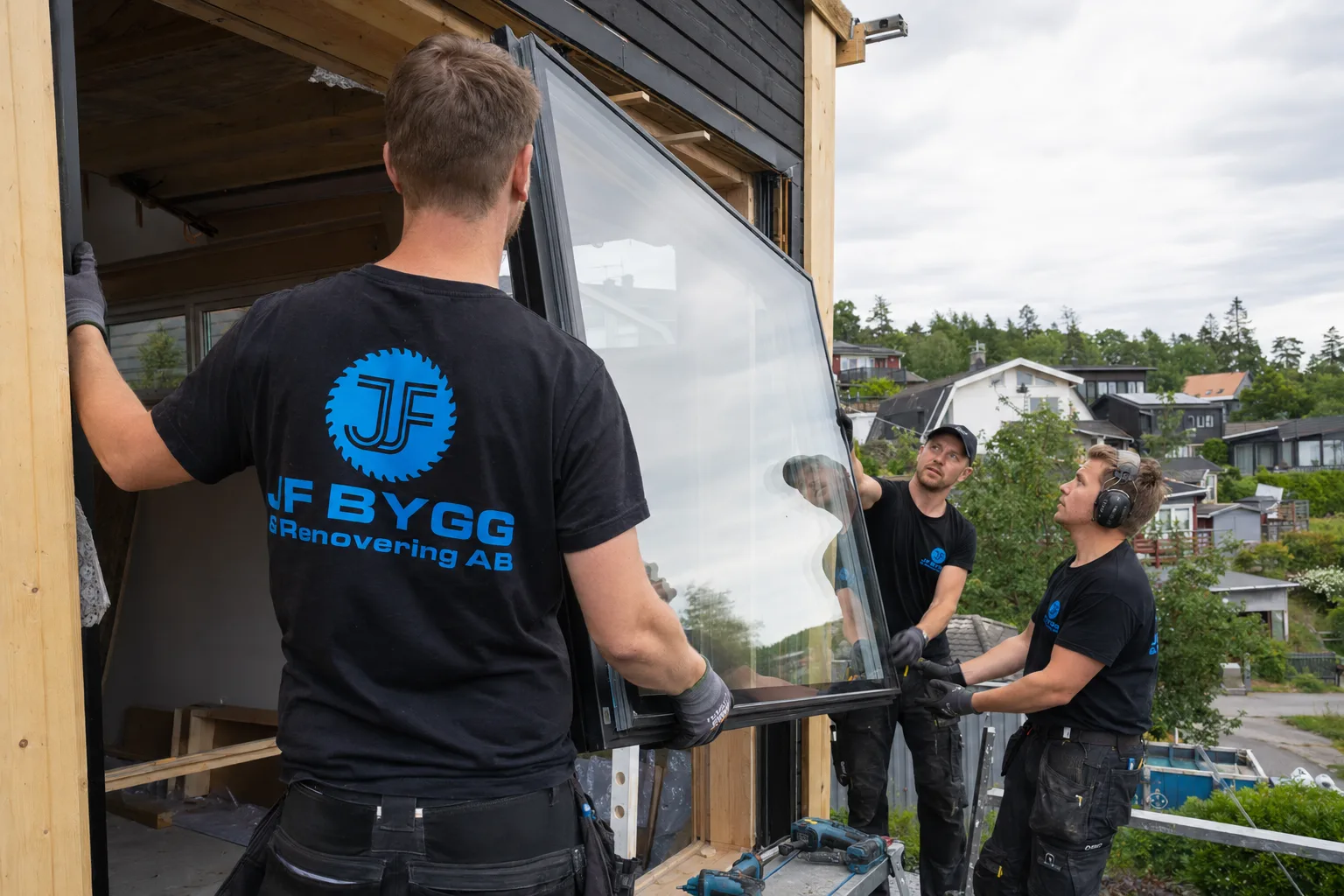 Tre arbetare installerar stora fönster i ett hus under renovering