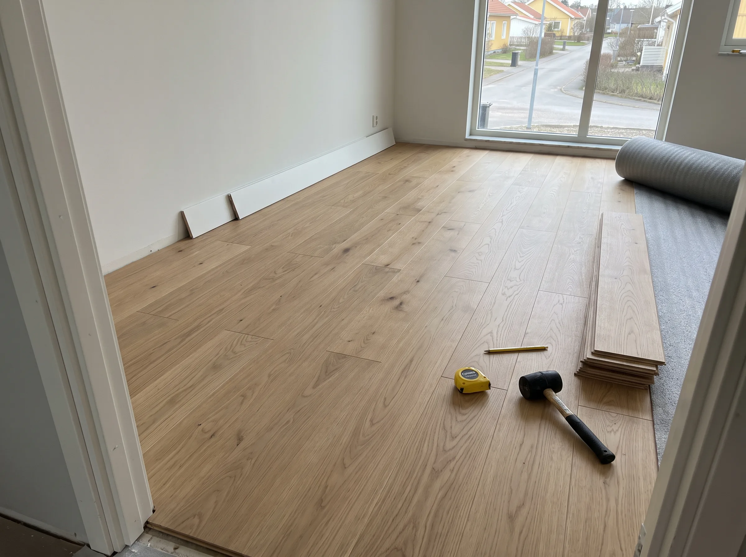 Nybyggd trägolvinstallation i ett rum med stora fönster som ger gott om ljus