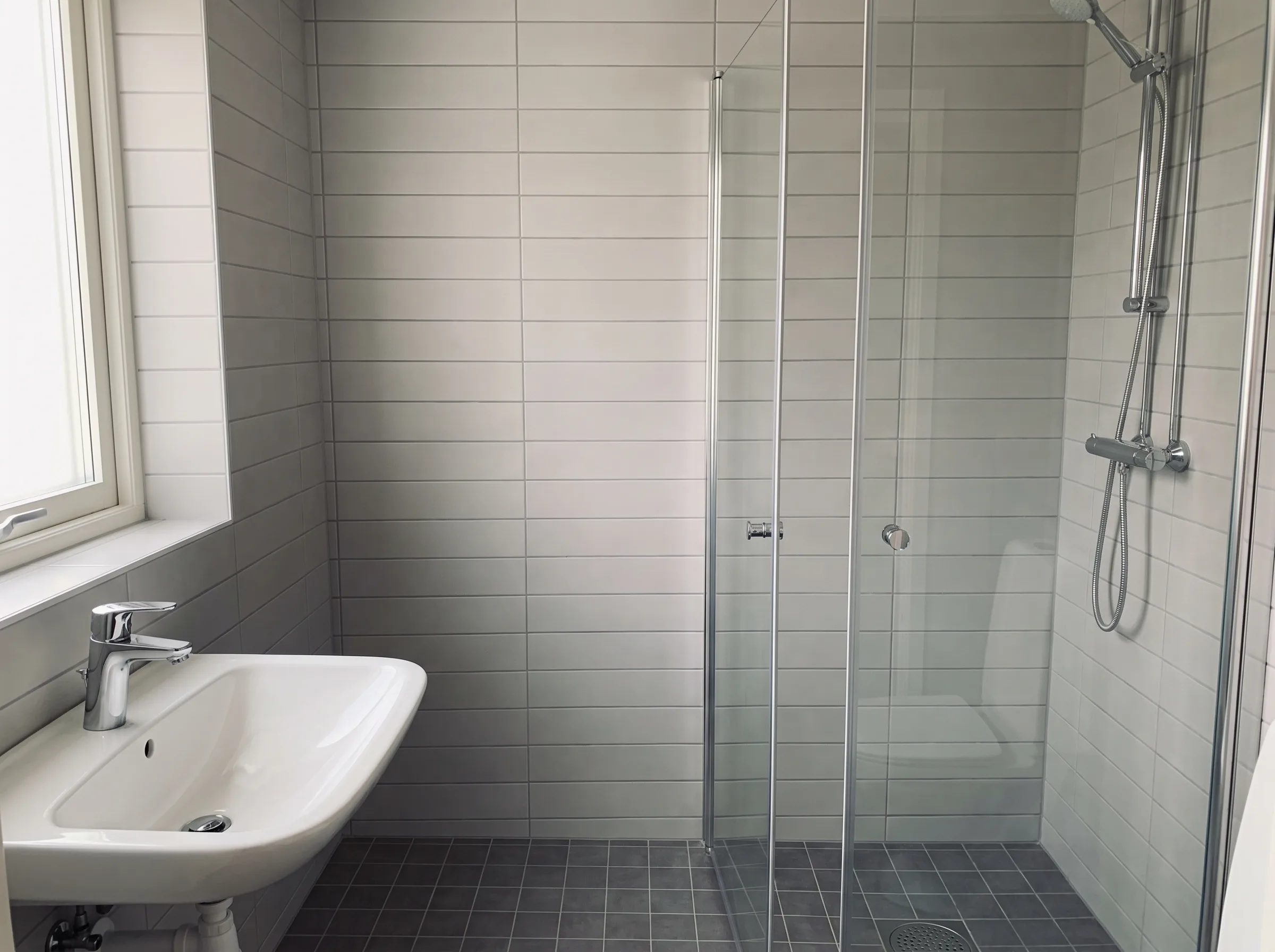 Nyrenoverat badrum med dusch och handfat, stilren design med ljusa kakelplattor