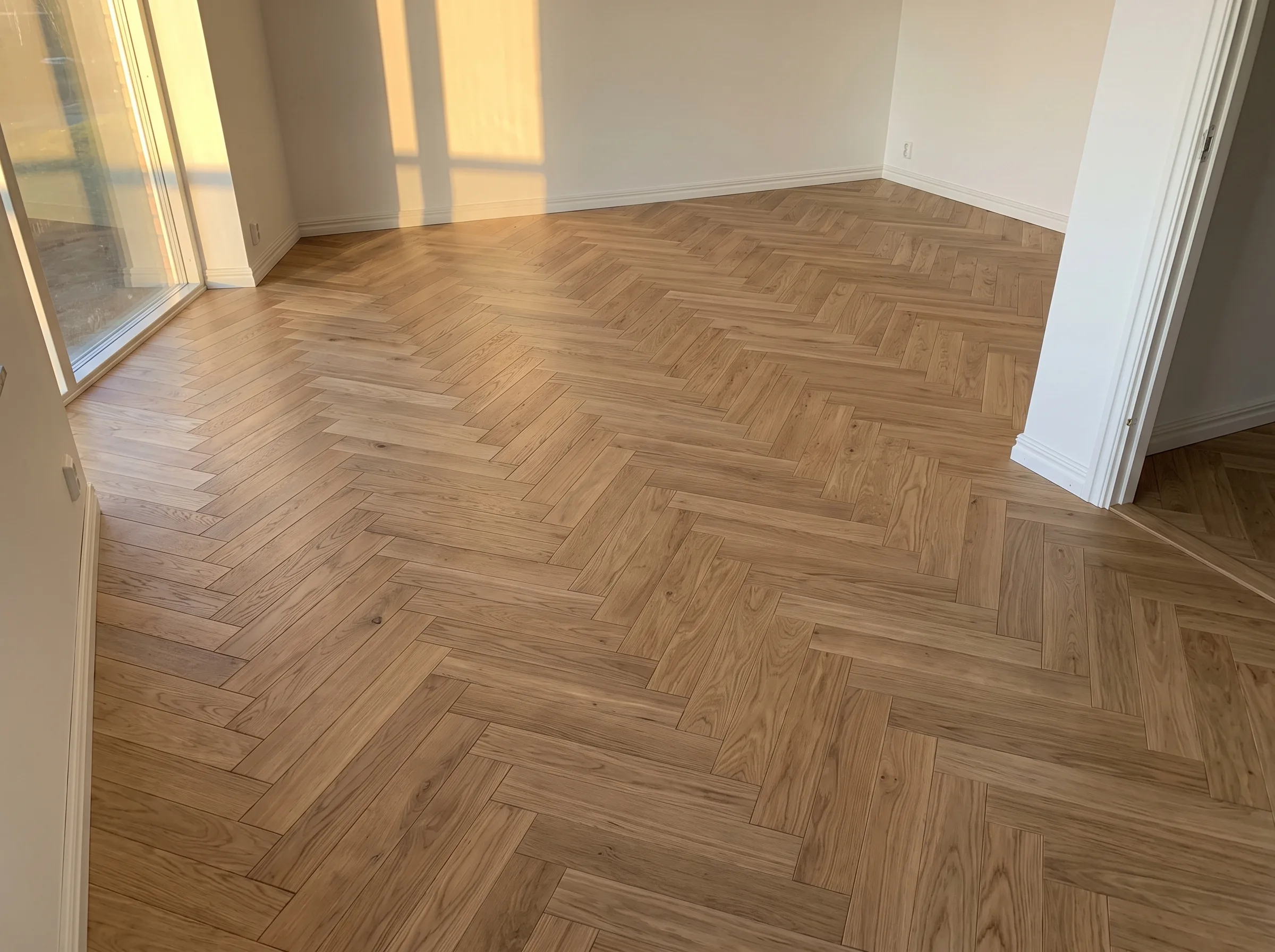 Nytt trägolv i fiskbensmönster installerat i ett ljust rum