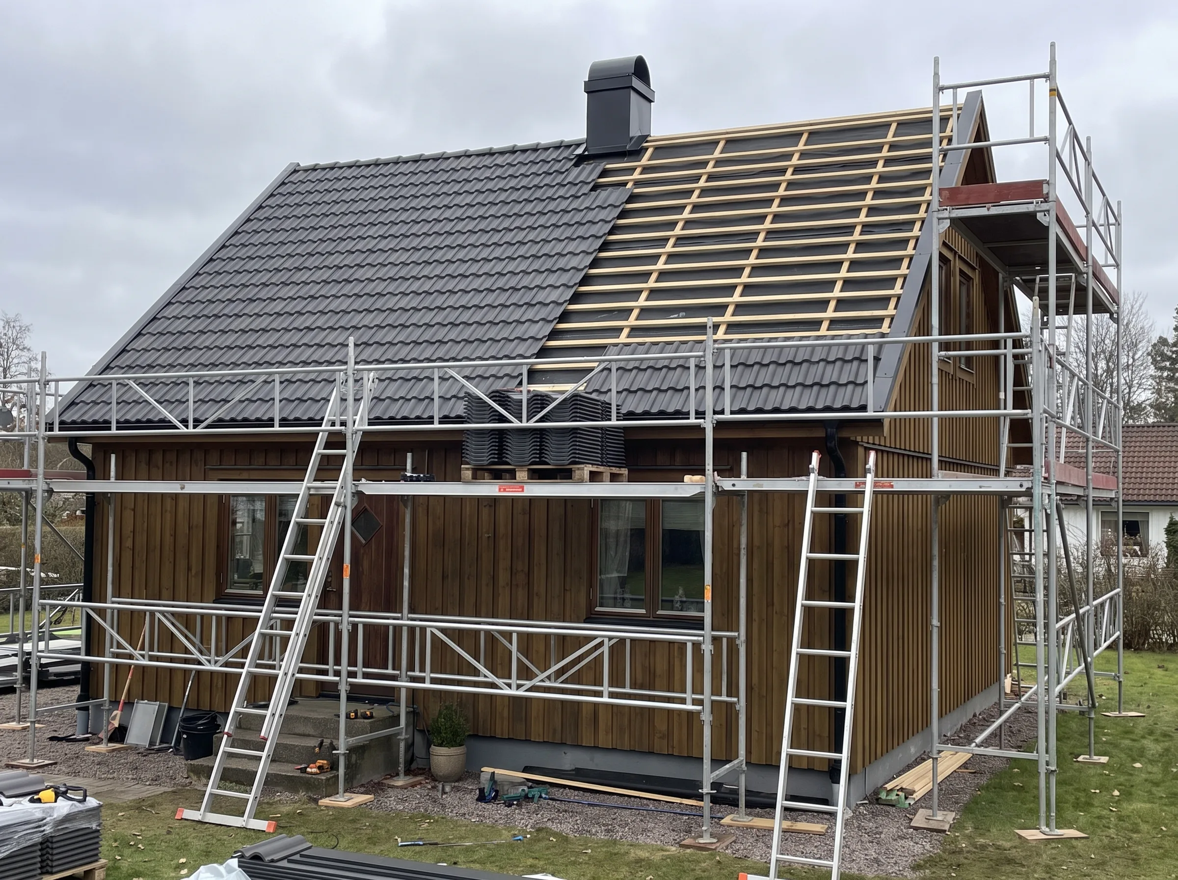 På bilden syns ett hus under takrenovering med ställningar och byggmaterial