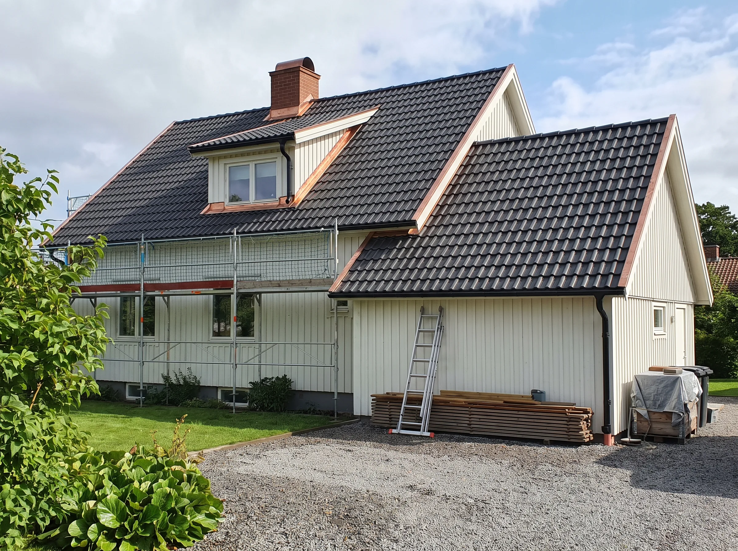Fasadarbete på ett hus med nytt tak och scaffolding. Grönska i förgrunden