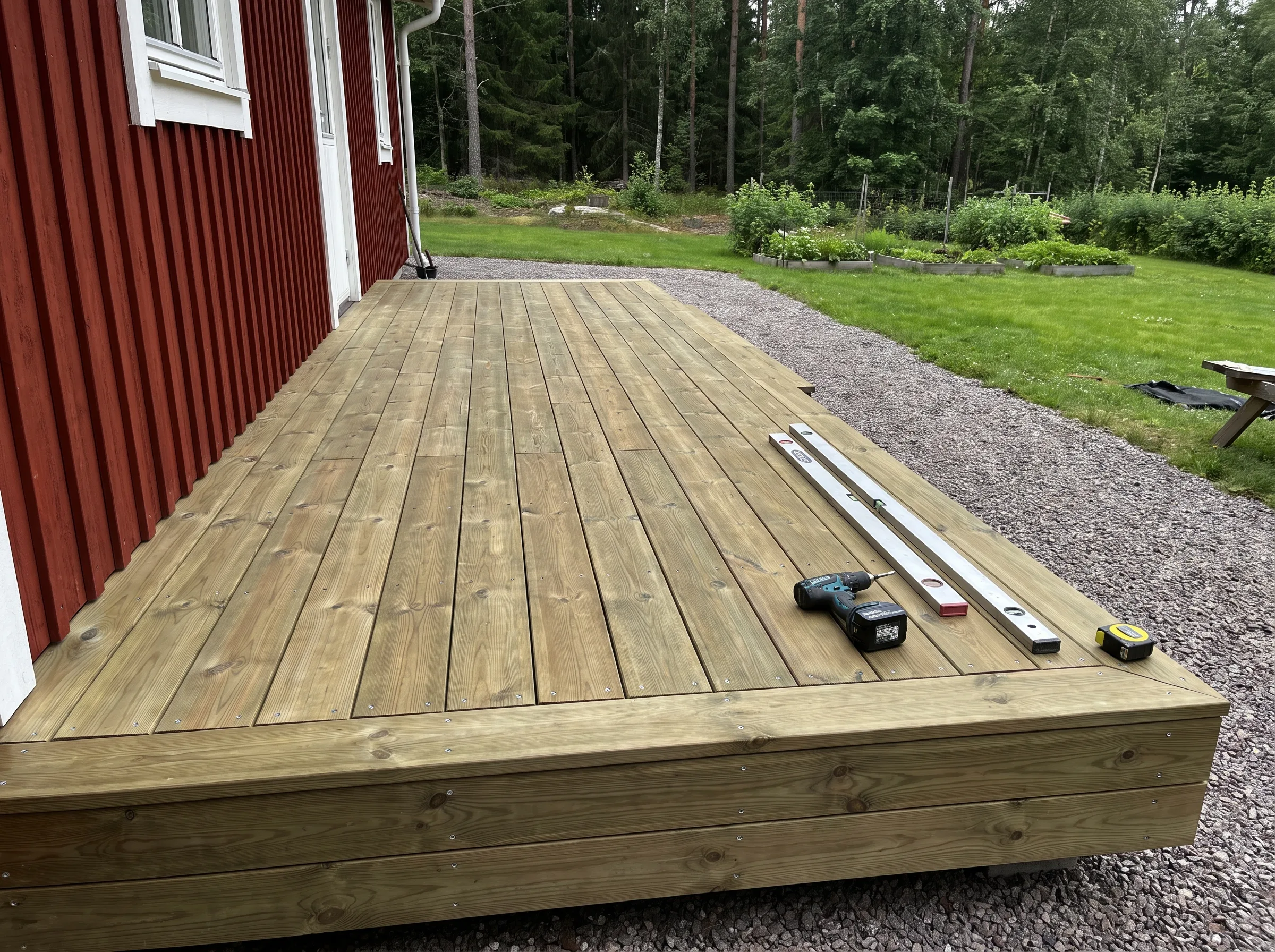 Nybyggd trädäck med verktyg på förgrunden, i en grönskande trädgård