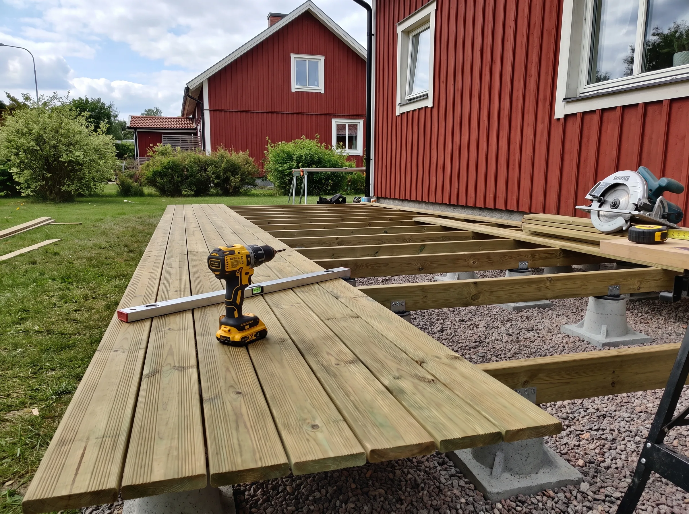 En trädäck byggs med verktyg och material i fokus, vid ett röd målat hus