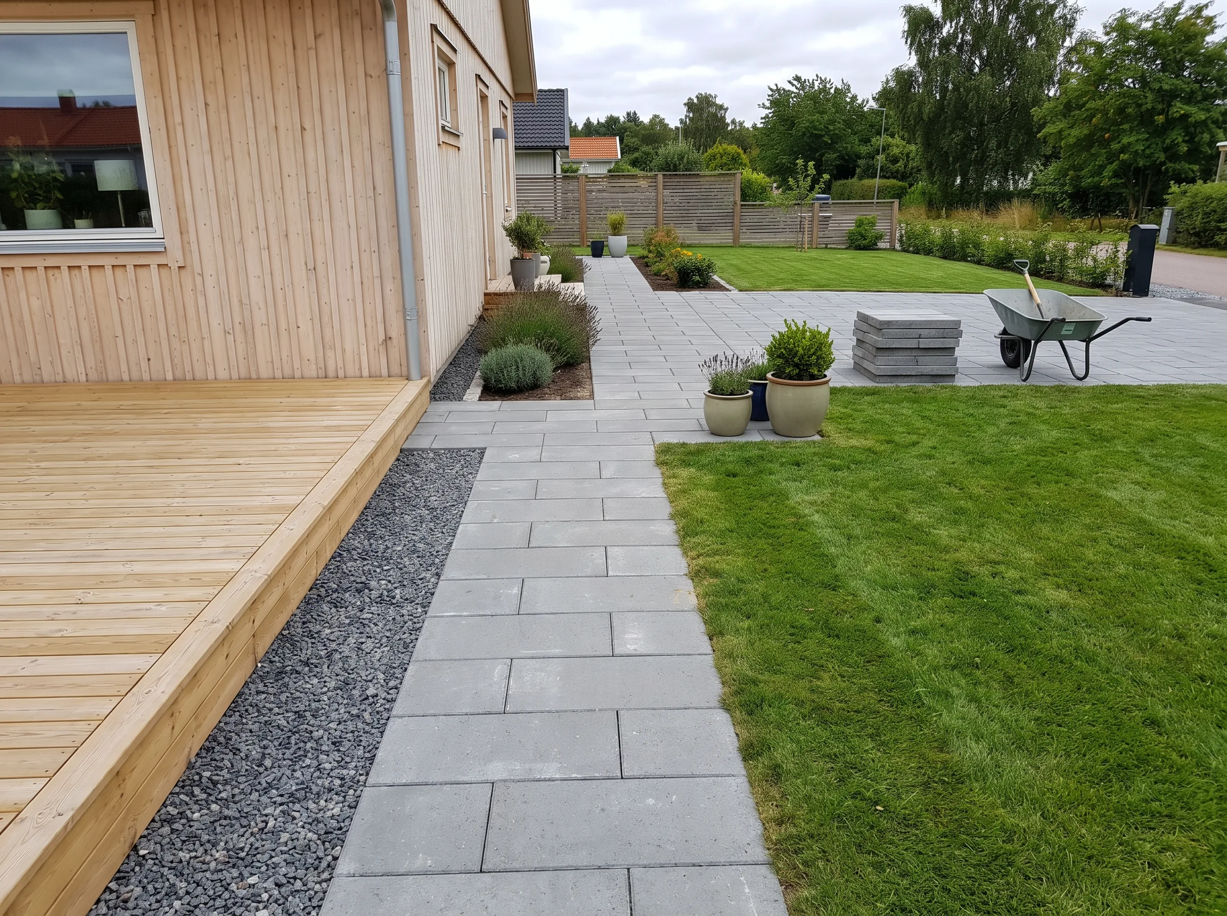 Utemiljö med stensättning, gräsmatta och altan i trä